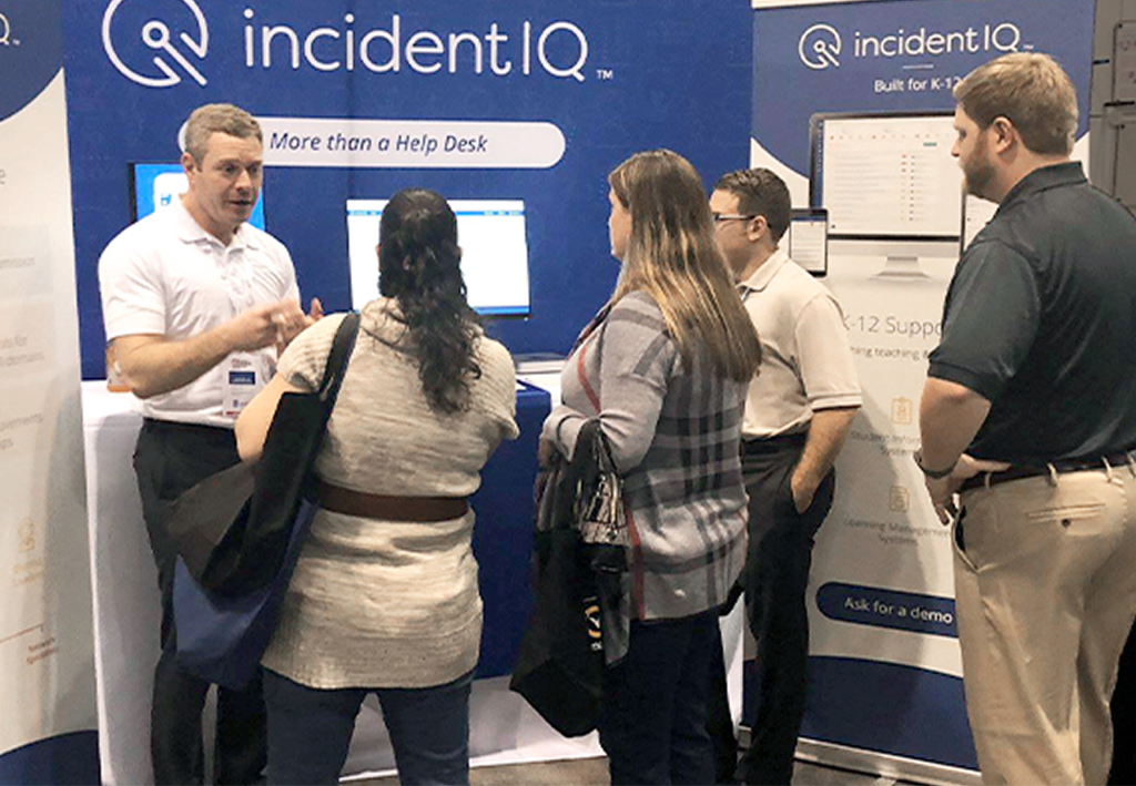 An Incident IQ representative talks with a group of people at a trade show.